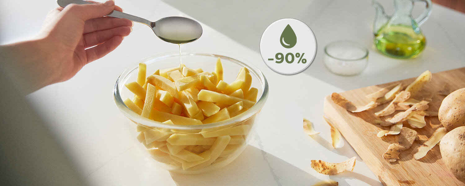 Na blacie kuchennym znajduje się miska z pokrojonymi ziemniakami, nad którą trzymana jest łyżka z olejem. Obok widoczna jest deska z obierkami ziemniaków i ikonka z napisem \'-90%\'.