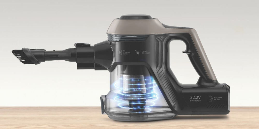 Bezprzewodowy odkurzacz ręczny w kolorze czarnym z przezroczystym pojemnikiem na kurz, na drewnianej powierzchni. Na urządzeniu widoczne są napisy: \'22.2V\' oraz \'REMOVABLE BATTERY\'.
