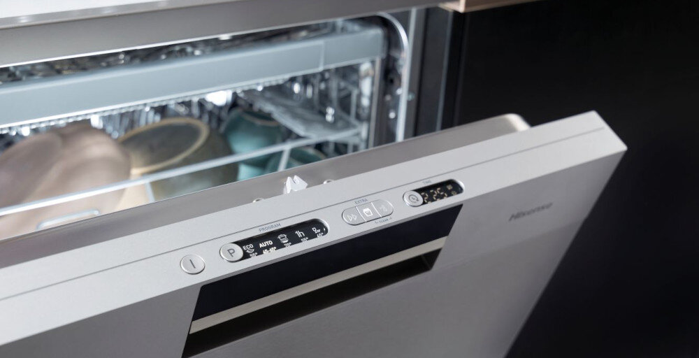 Otwarta zmywarka z widocznym panelem sterowania, na którym znajdują się przyciski i wyświetlacz. Wewnątrz zmywarki widać naczynia i sztućce.