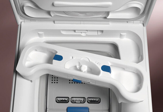 Wnętrze pralki z widocznym pojemnikiem na detergenty, który ma białą obudowę z niebieskimi elementami. W tle widać otwartą pokrywę pralki.