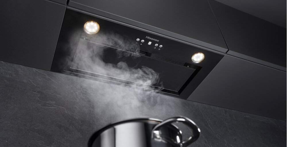 Czarny okap kuchenny z logo Hisense zamontowany w szafce, z dwoma włączonymi światłami. Pod okapem unosi się para z gotującego się garnka.