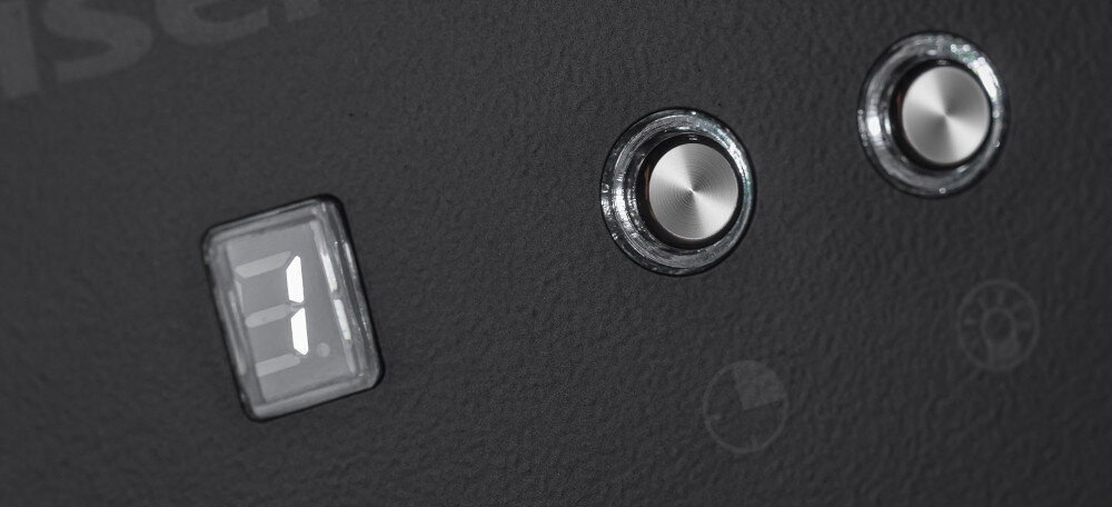 Na czarnym panelu widoczny jest wyświetlacz z cyfrą \'1\' oraz dwa okrągłe przyciski z metalicznym wykończeniem.