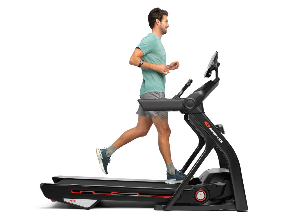 Mężczyzna biegnie na bieżni elektrycznej marki Bowflex. Na bieżni widoczne jest logo \'BOWFLEX\'.