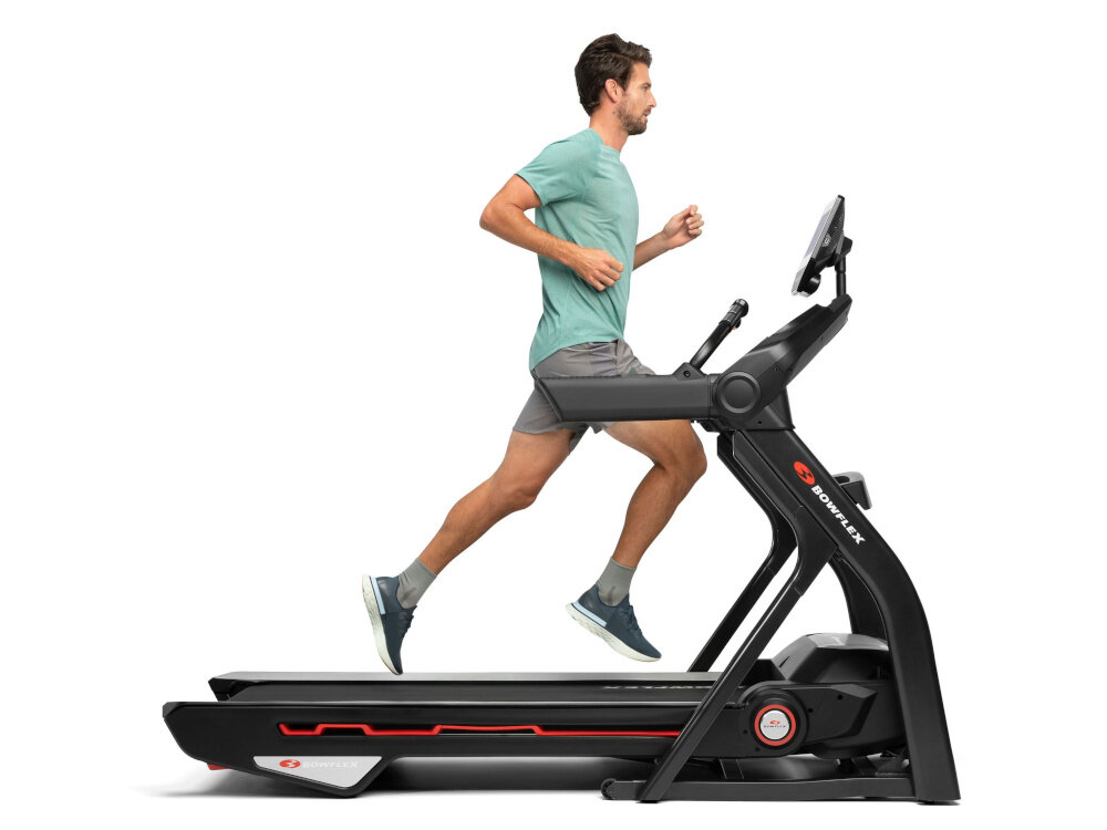 Mężczyzna biegnie na bieżni elektrycznej z widocznym logo \'BOWFLEX\'. Bieżnia ma czarną konstrukcję z czerwonymi akcentami i ekranem przed użytkownikiem.