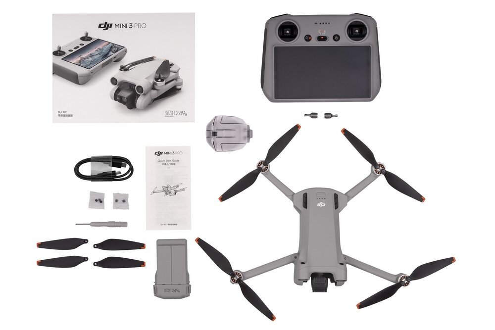 Na obrazie znajduje się zestaw drona DJI Mini 3 Pro RC, w skład którego wchodzą dron, kontroler, śmigła, kabel, instrukcja oraz inne akcesoria. Widoczne jest logo DJI na opakowaniu i dronie.