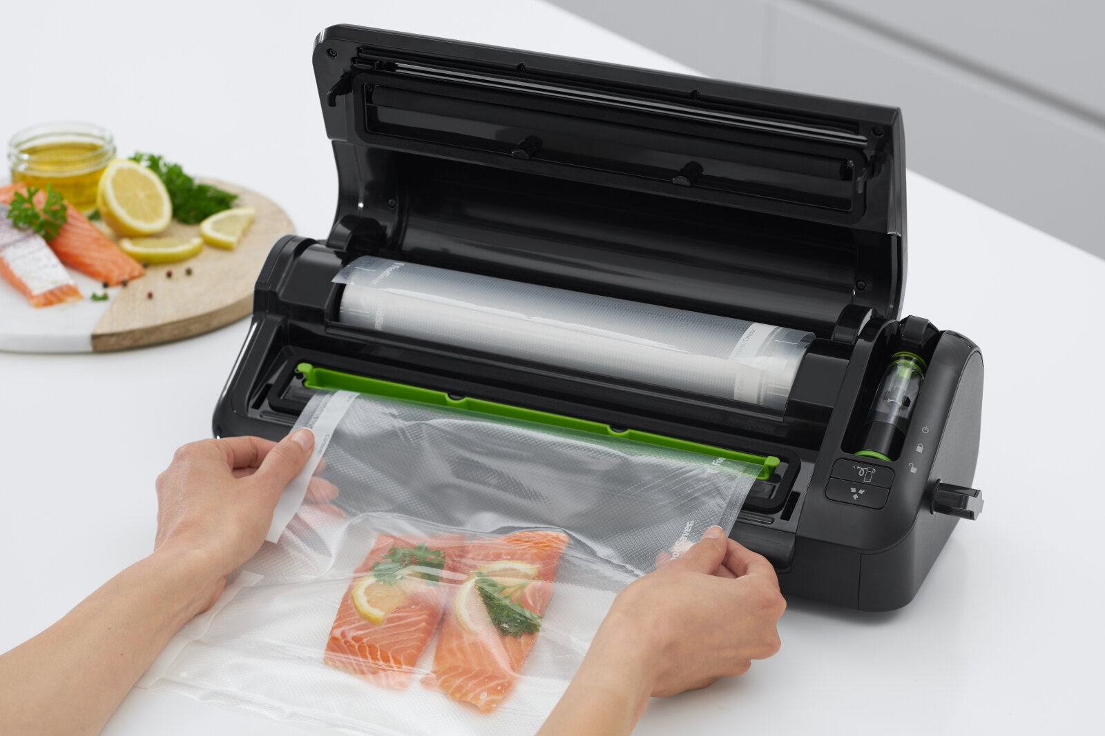 Osoba używa zgrzewarki próżniowej do pakowania kawałków łososia w przezroczystą folię. W tle widoczny jest talerz z plasterkami cytryny i kawałkami łososia.