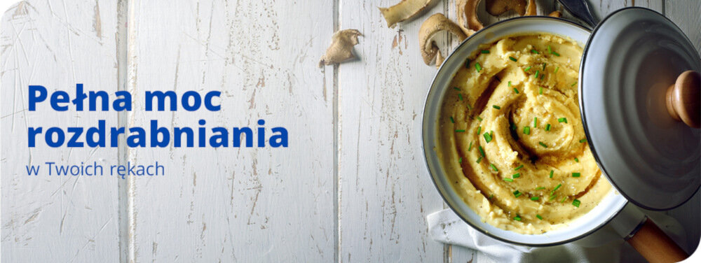 Na białym drewnianym tle znajduje się garnek z kremową potrawą posypaną ziołami. Obok widoczny jest tekst: \'Pełna moc rozdrabniania w Twoich rękach\'.