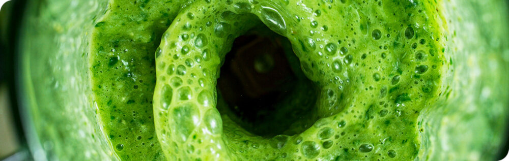 Zbliżenie na wirujący zielony koktajl w blenderze, z widocznymi bąbelkami powietrza na powierzchni.