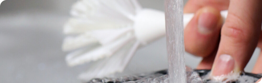 Osoba myje czarną powierzchnię pod bieżącą wodą, używając białej szczotki.