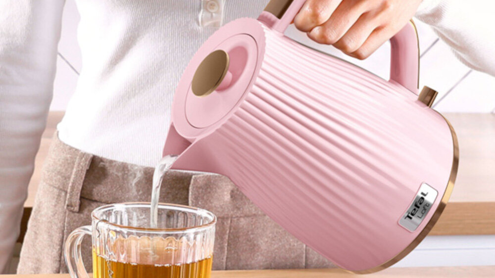 Osoba nalewa wodę z różowego czajnika do szklanki. Na czajniku widoczne jest logo \'Tefal\'.