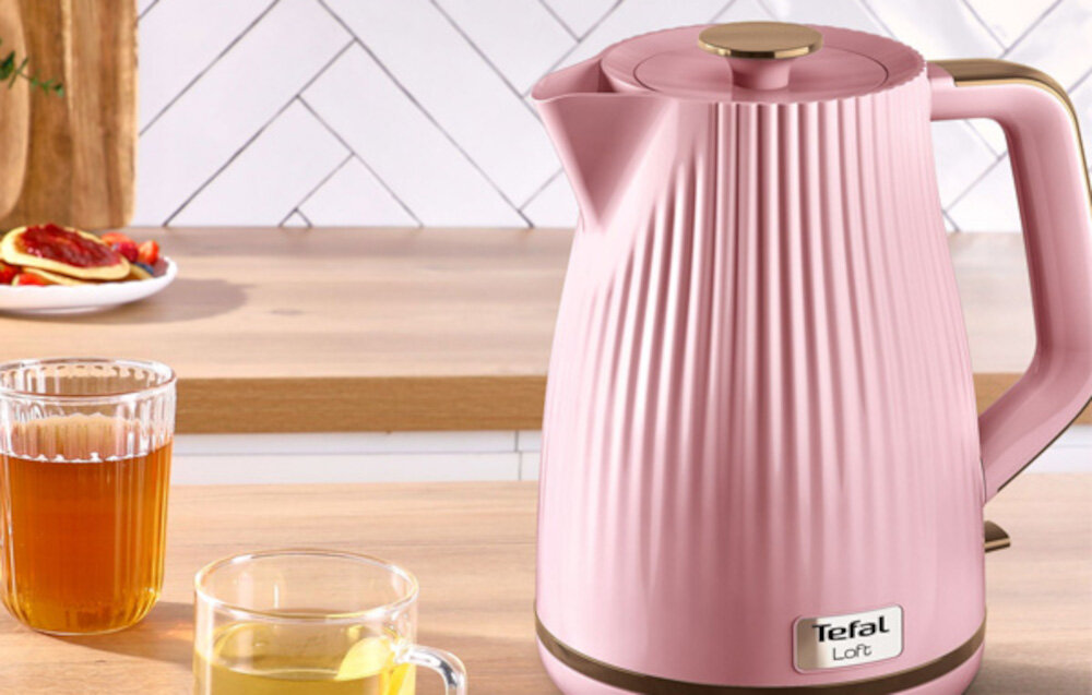 Różowy czajnik z pionowymi żłobieniami stoi na blacie kuchennym. Na czajniku widoczne jest logo \'Tefal Loft\'.