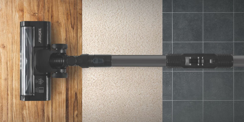 Odkurzacz z logo \'Zelmer\' na głowicy, widoczny na trzech różnych powierzchniach: drewnianej, dywanowej i kafelkowej.