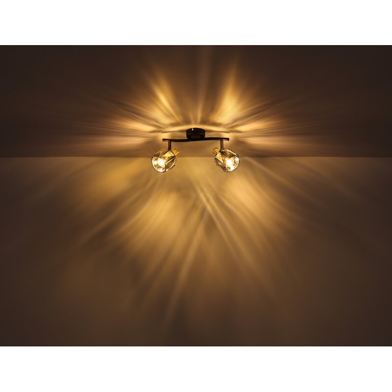 Na obrazie widoczna jest lampa sufitowa z dwoma źródłami światła, które emitują ciepłe, rozproszone światło na sufit i ścianę. Lampa ma szklane, przydymione kryształy, które tworzą efektowne wzory świetlne.