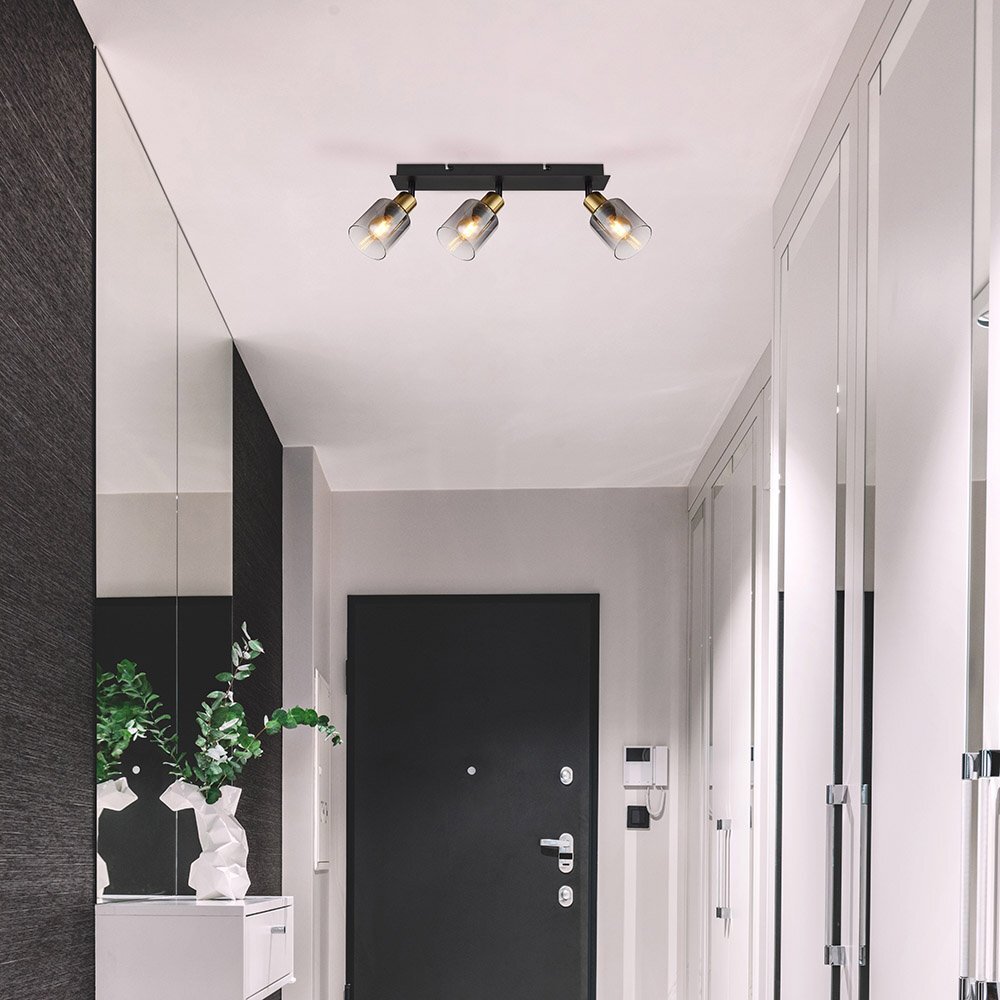 Na suficie zamontowana jest lampa sufitowa z trzema reflektorami o przydymionych szklanych kloszach. Wnętrze pomieszczenia jest nowoczesne, z ciemnymi drzwiami i jasnymi ścianami.