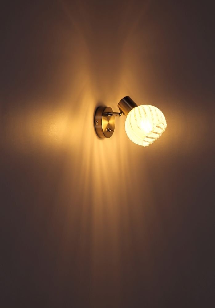 Na obrazie widoczny jest włączony reflektor ścienny emitujący ciepłe, rozproszone światło na ścianę. Reflektor ma metaliczną podstawę i szklany klosz.