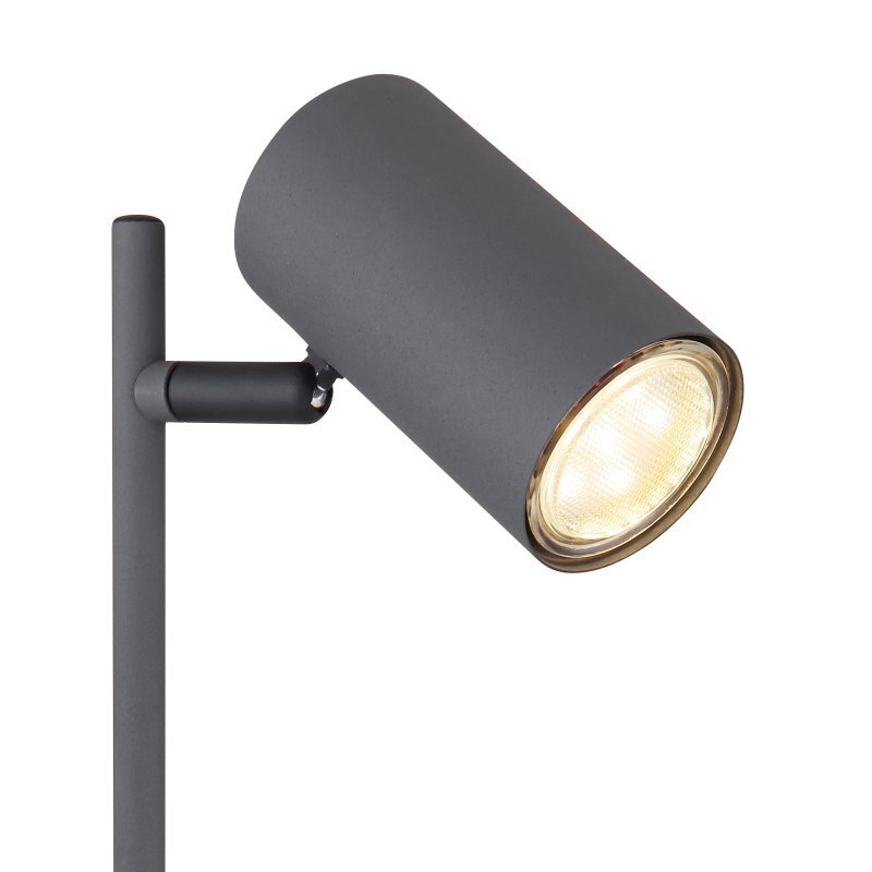 Metalowa lampa stołowa w kolorze grafitowym z cylindrycznym kloszem, emitująca ciepłe światło. Klosz zamocowany jest na prostym ramieniu.