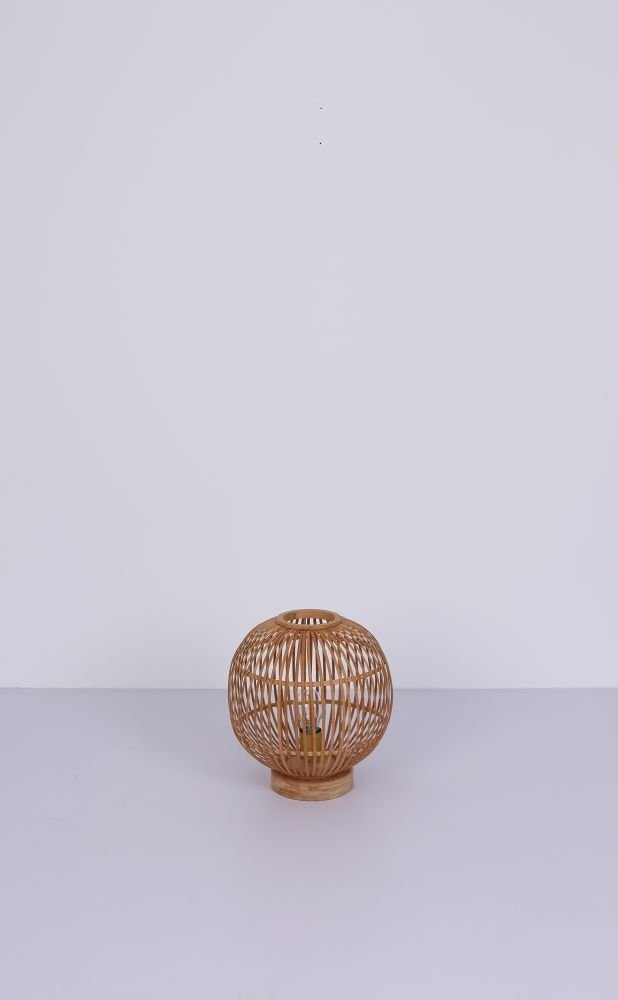Na obrazie widoczna jest lampa stołowa wykonana z naturalnego bambusa, o kulistym kształcie z ażurową konstrukcją. Lampa stoi na jasnym tle, a jej wnętrze jest puste, co pozwala na widoczność żarówki.