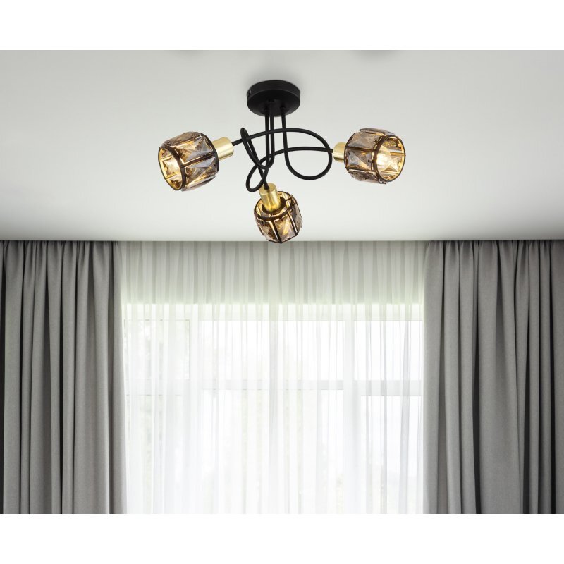 Na suficie zamontowana jest lampa z trzema żarówkami, każda w oprawie z dymionego szkła i złotymi elementami. W tle widoczne są zasłony i okno z firaną.
