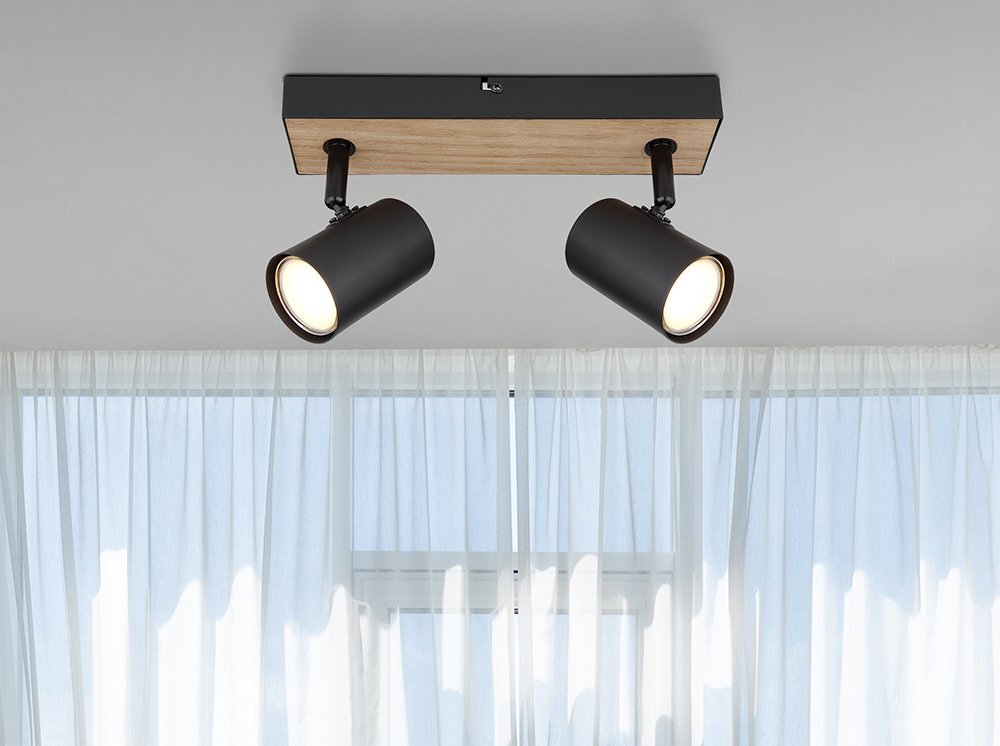 Lampa sufitowa z dwoma czarnymi reflektorami zamontowana na prostokątnej podstawie z imitacji drewna. W tle widoczne są białe, półprzezroczyste zasłony.