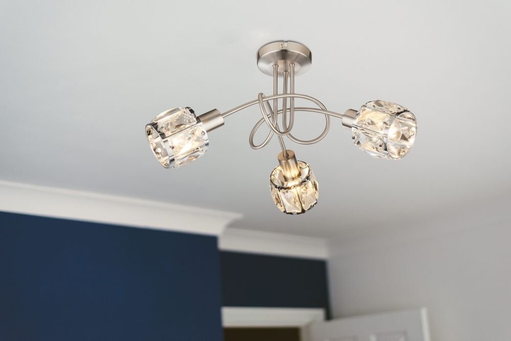 Na obrazie widoczna jest lampa sufitowa z trzema źródłami światła, wykonana z chromowanej satyny i szklanych kryształów. Lampa jest zamontowana na suficie w pomieszczeniu z niebieską ścianą i białym sufitem.