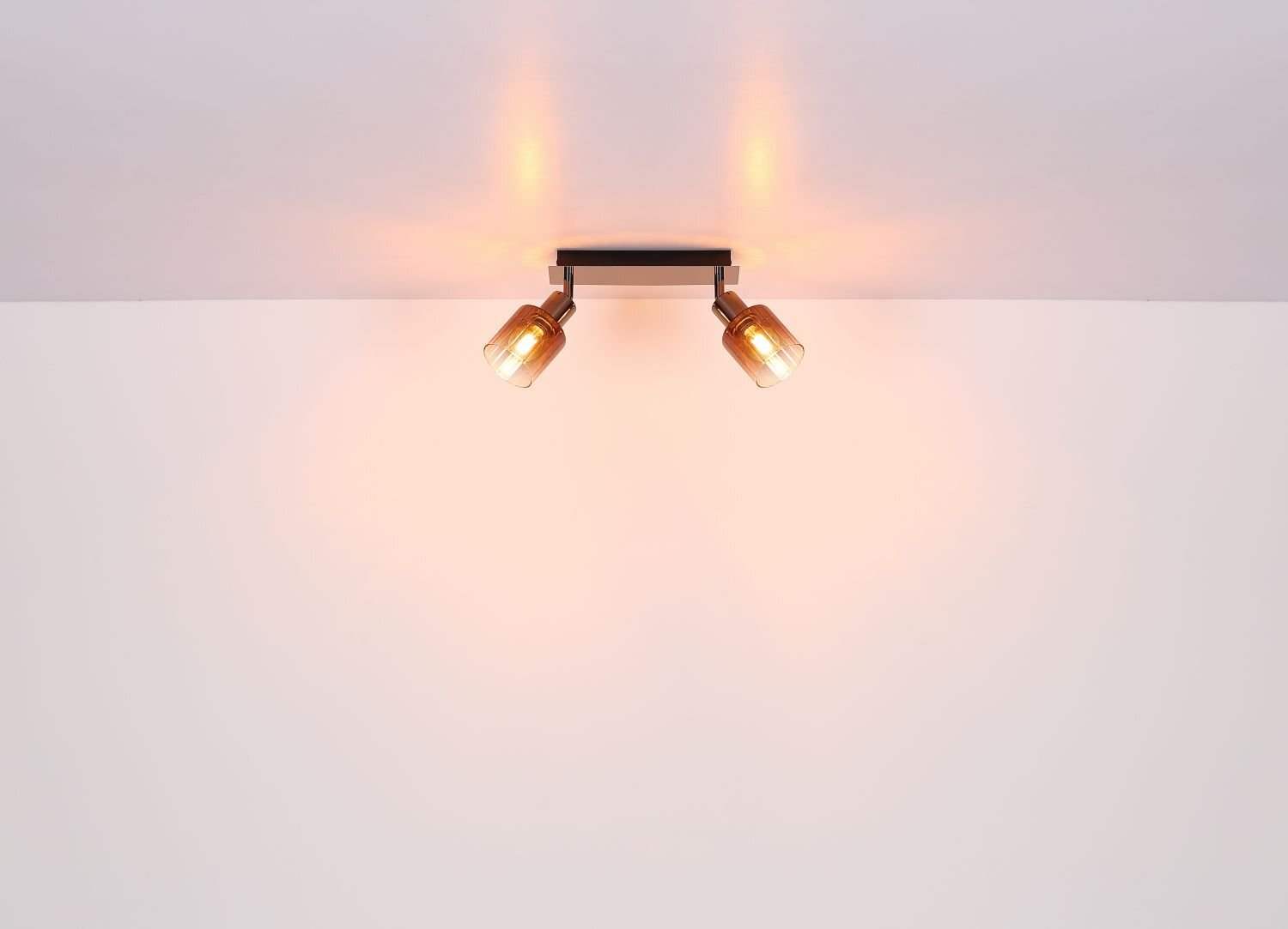 Na obrazie widoczna jest lampa sufitowa z dwoma reflektorami emitującymi ciepłe światło. Lampa zamontowana jest na białym suficie.