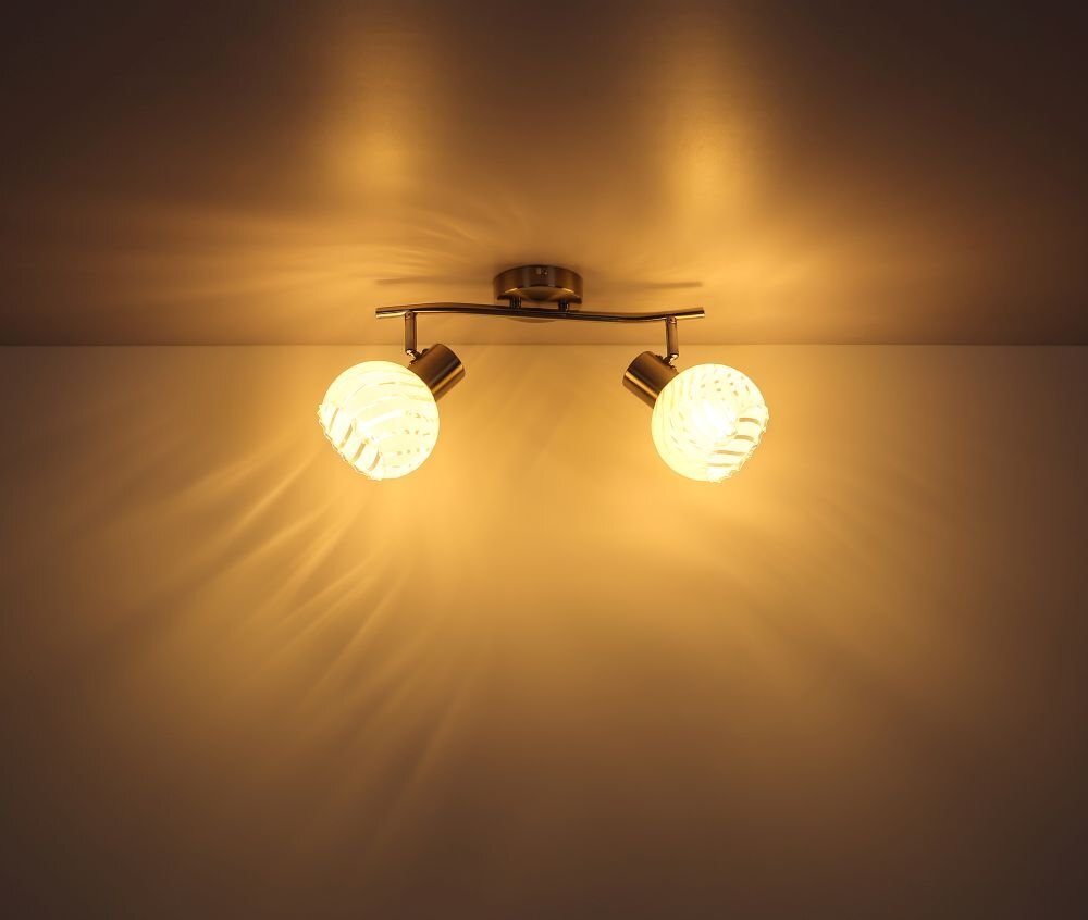 Na obrazie widoczny jest sufitowy reflektor z dwoma źródłami światła, które emitują ciepłe, żółte światło. Reflektor ma metalowe elementy w kolorze satyny i białe szklane klosze.