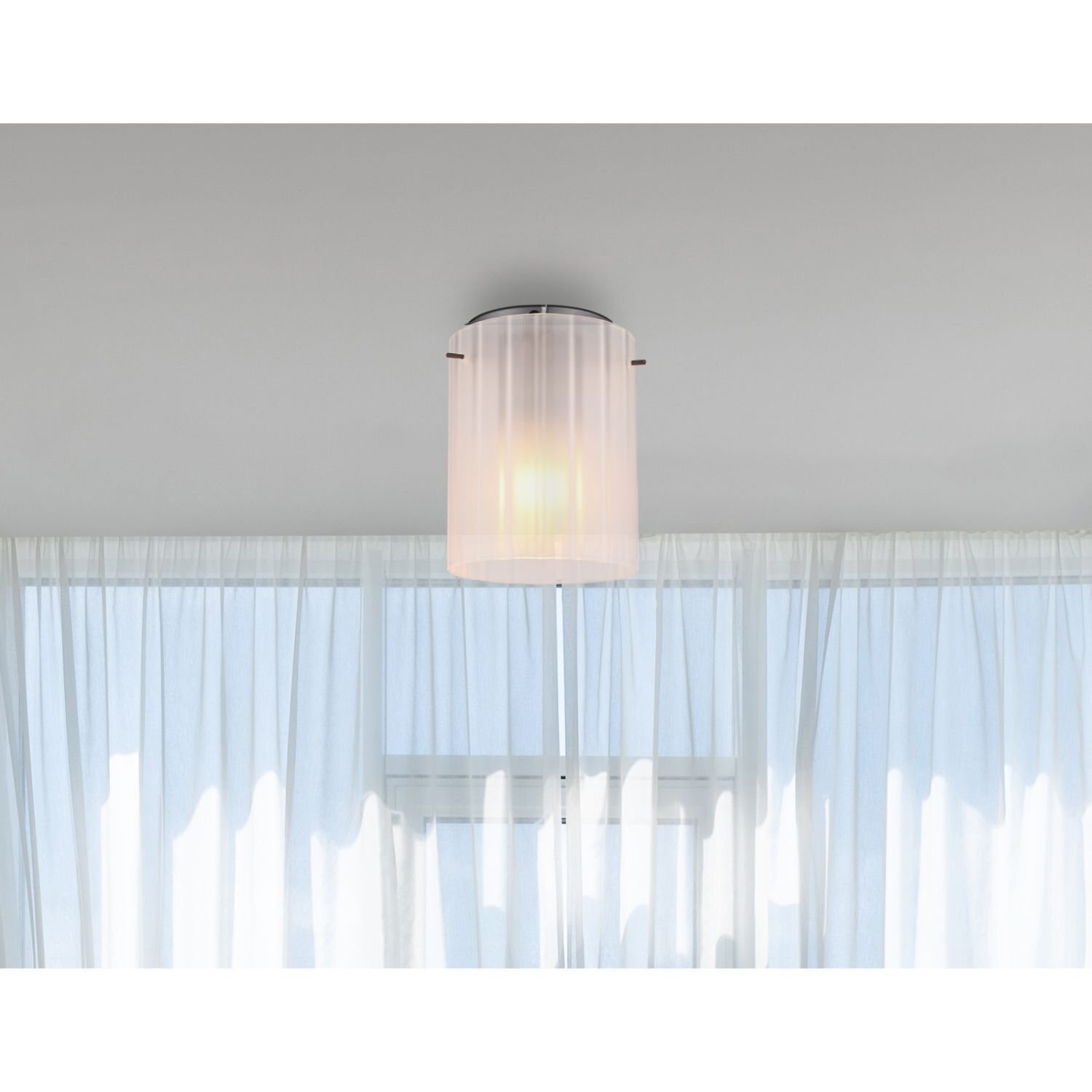 Na obrazie widoczna jest lampa sufitowa z ryflowanym kloszem, zamontowana na suficie. W tle znajdują się zasłony przepuszczające światło dzienne.