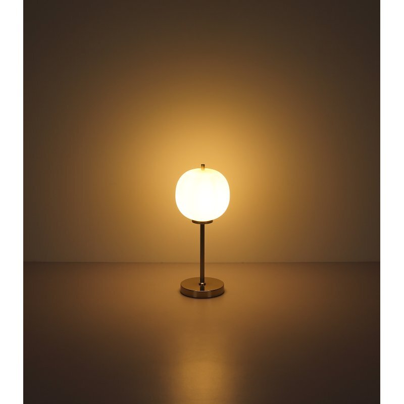 Na obrazie widoczna jest lampa stołowa z okrągłym, opalowym kloszem emitującym ciepłe światło. Lampa stoi na metalowej podstawie w matowym niklu.