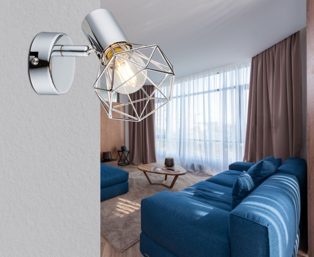 Na ścianie zamontowany jest chromowany reflektor z geometrycznym kloszem, w którym widoczna jest żarówka. W tle znajduje się nowoczesny salon z dużymi oknami, niebieskimi sofami i stolikiem kawowym.