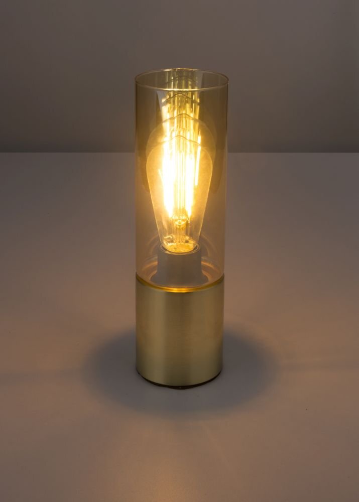 Złota lampa stołowa z bursztynowym szkłem, w której widoczna jest zapalona żarówka. Lampa stoi na gładkiej powierzchni.