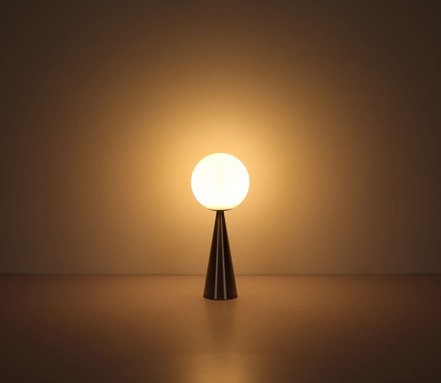 Na obrazie widoczna jest lampa stołowa z kulistym kloszem emitującym ciepłe, żółte światło. Podstawa lampy ma kształt stożka i jest wykonana z ciemnego materiału.