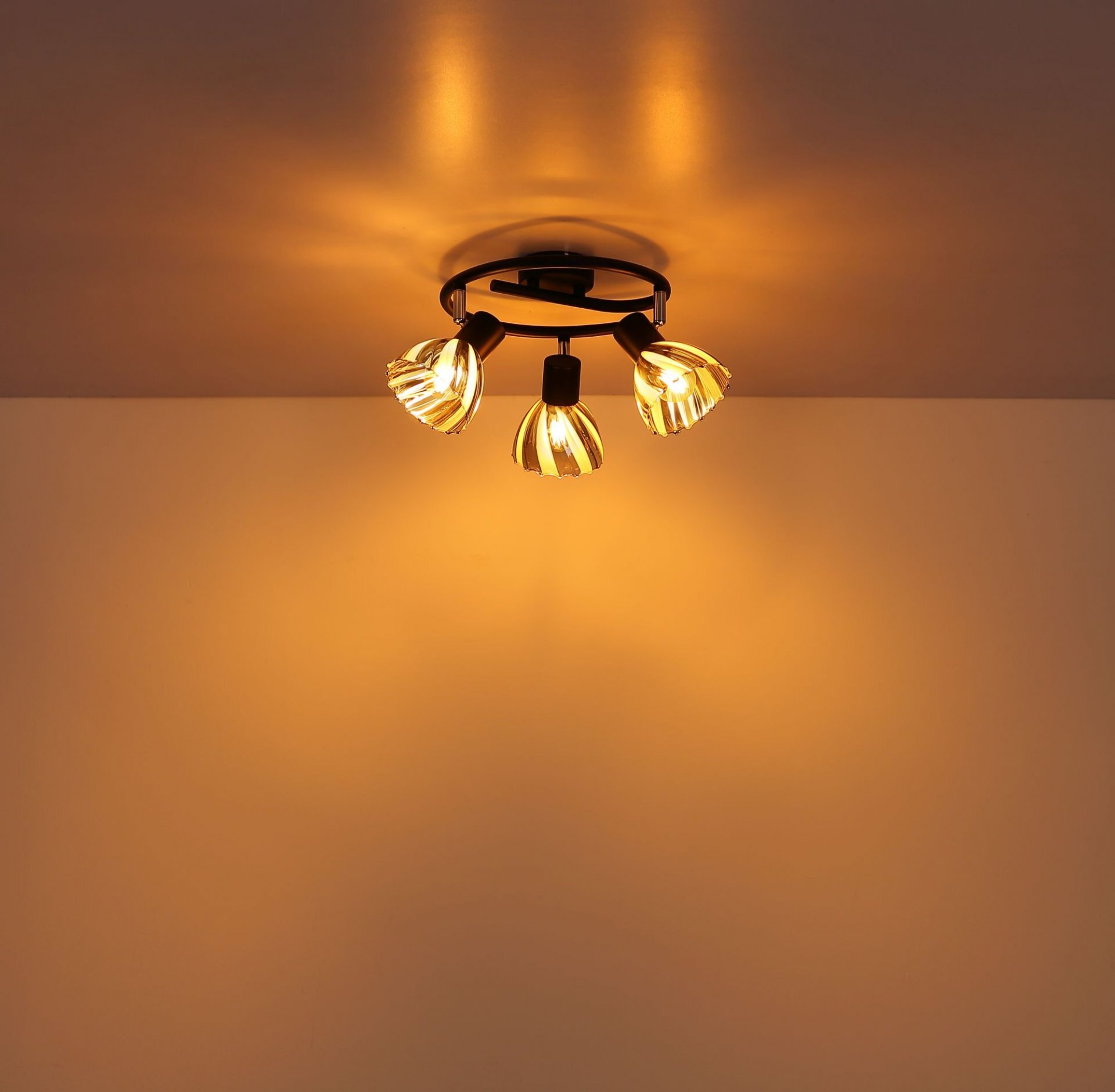 Na suficie zamontowana jest nowoczesna lampa sufitowa z trzema regulowanymi reflektorami, które emitują ciepłe, żółte światło. Reflektory mają dekoracyjne klosze z przezroczystymi i złotymi elementami.
