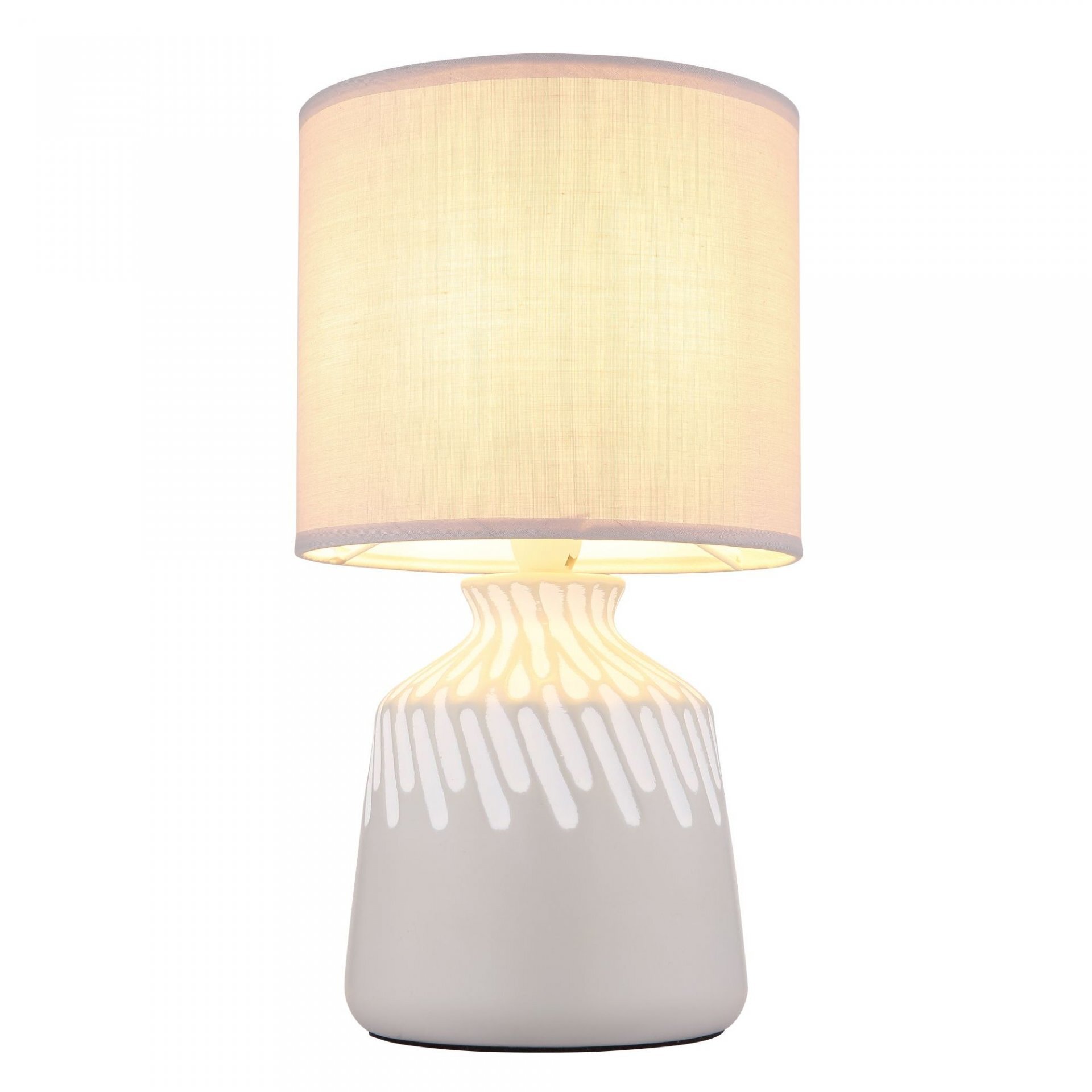 Na obrazie widoczna jest lampa stołowa z jasnym, cylindrycznym abażurem i ozdobną podstawą w białym kolorze z wzorem przypominającym krople. Lampa emituje ciepłe, rozproszone światło.