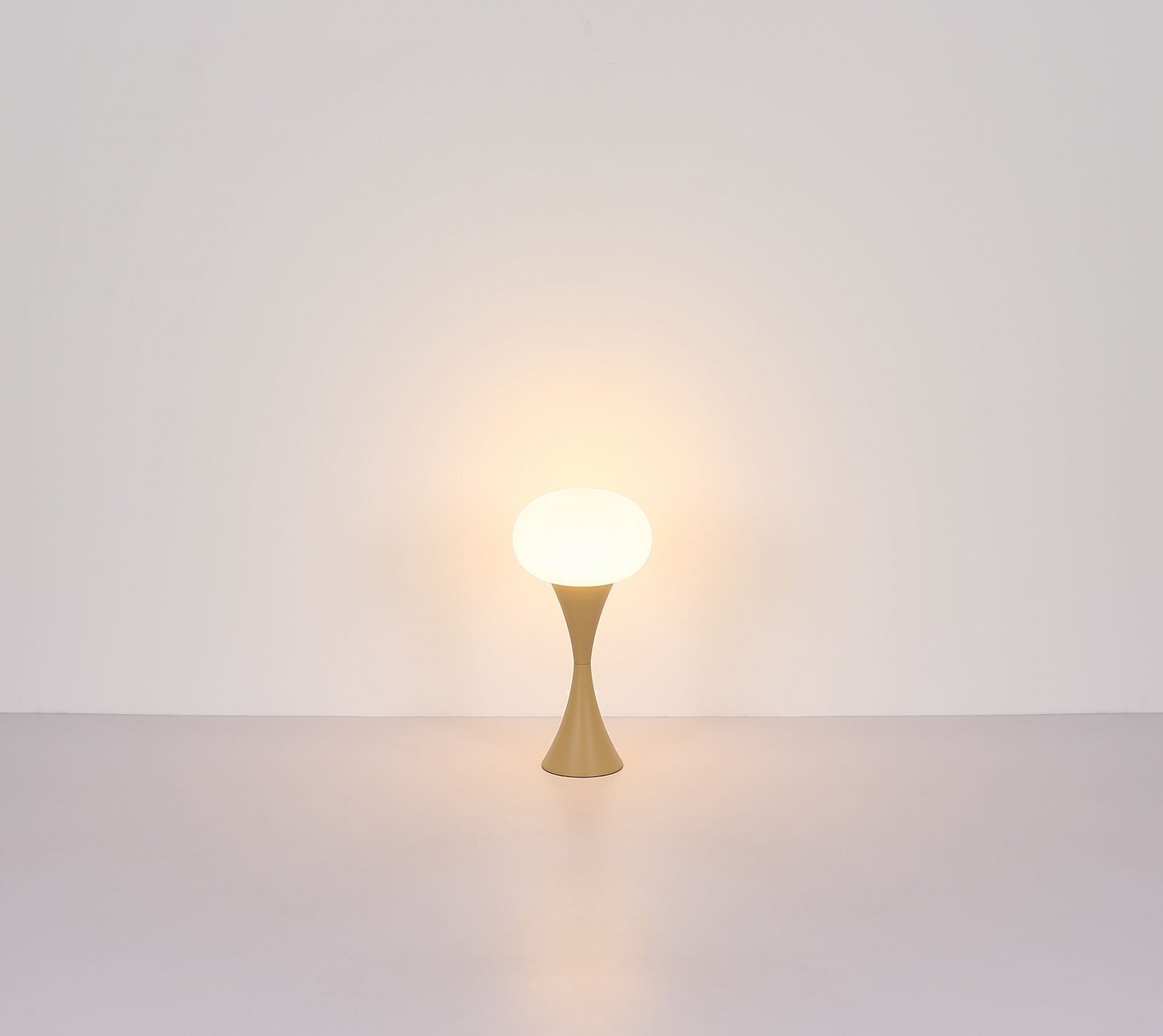 Na obrazie widoczna jest lampa stołowa z kulistym kloszem emitującym ciepłe światło, umieszczona na smukłej podstawie w jasnym kolorze. Tło jest jednolite i jasne.