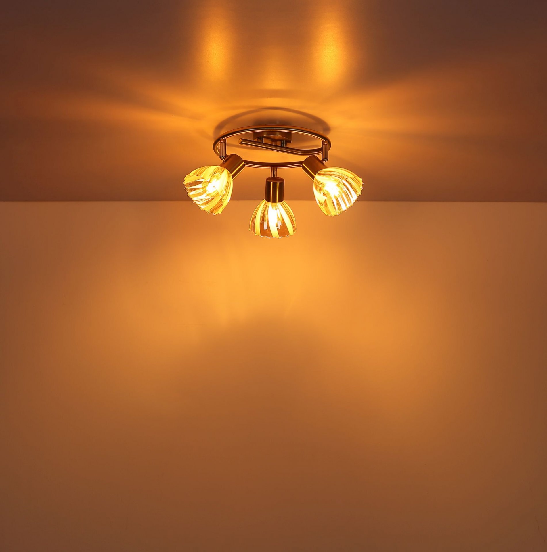 Na suficie zamontowana jest lampa sufitowa z trzema punktami świetlnymi, emitująca ciepłe, żółte światło. Światło tworzy wzory na suficie i ścianie.