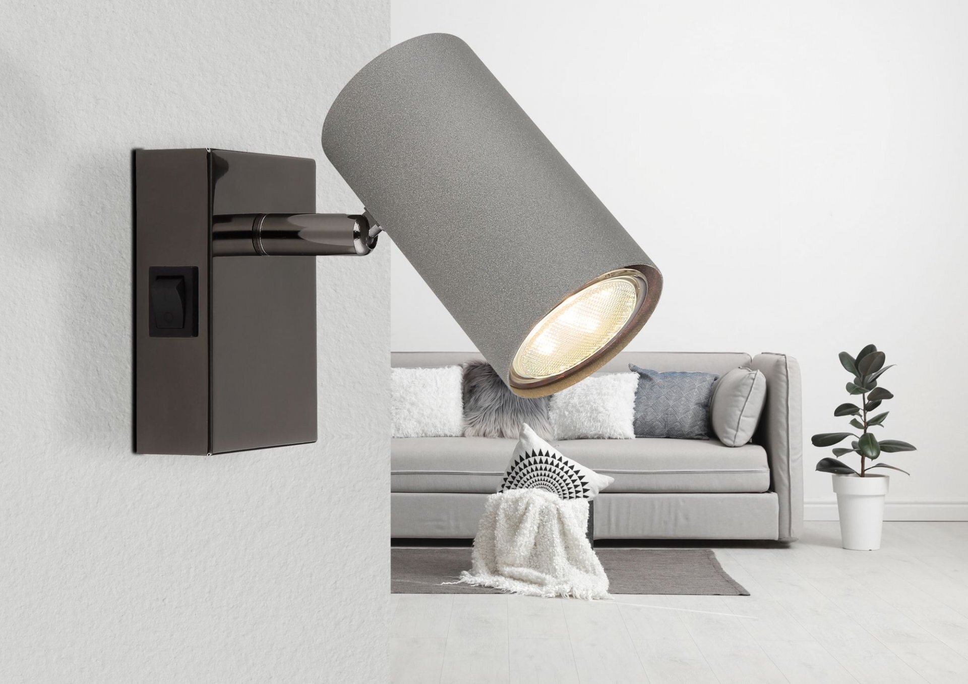 Na obrazie widoczna jest lampa reflektorowa zamontowana na ścianie, z włącznikiem na prostokątnej podstawie. W tle znajduje się jasna sofa z poduszkami i kocem oraz roślina w doniczce.