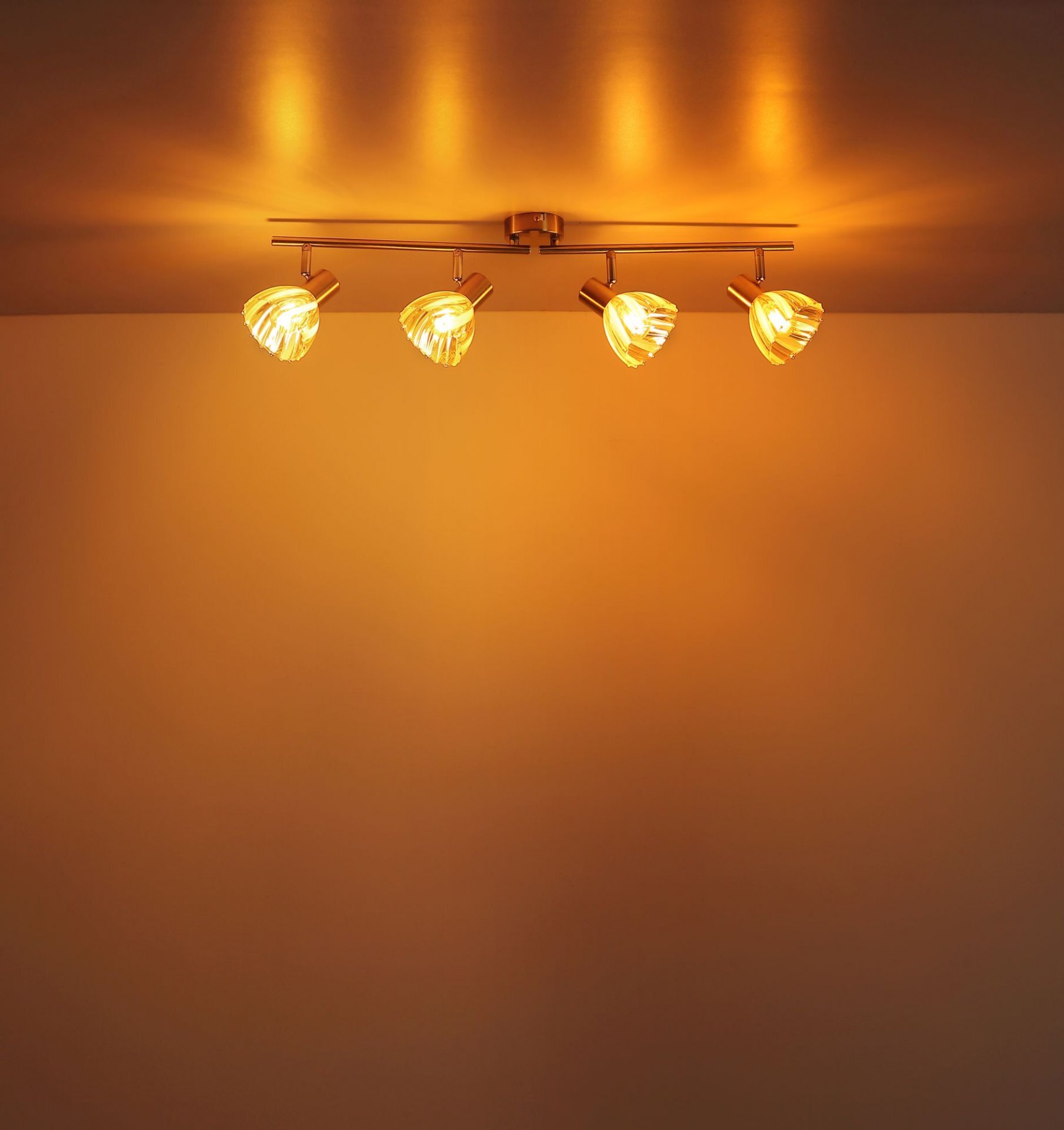 Na suficie zamontowana jest lampa z czterema regulowanymi reflektorami, emitująca ciepłe, żółte światło. Lampa ma nowoczesny design i metalową konstrukcję.