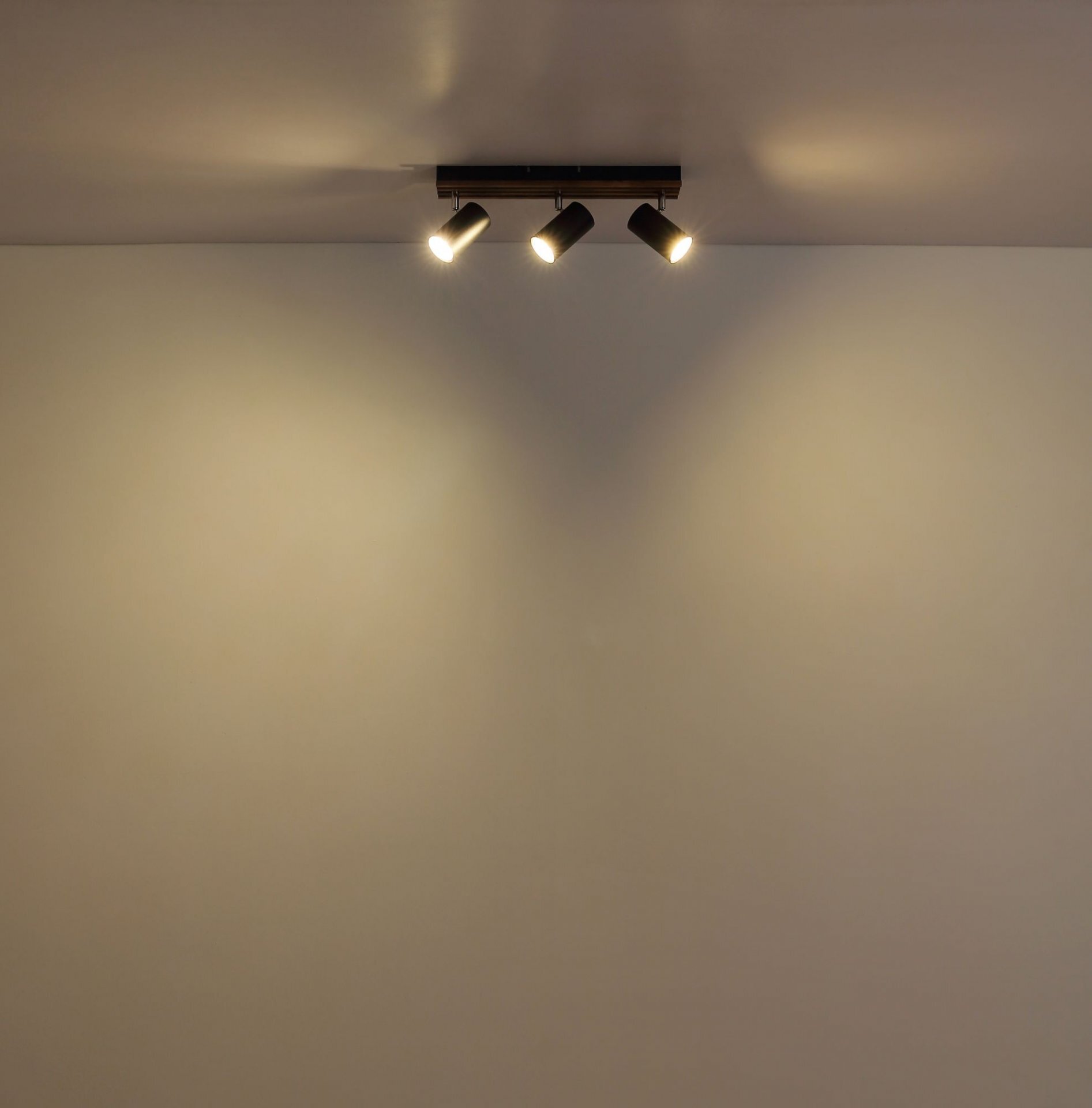 Na suficie zamontowana jest nowoczesna lampa sufitowa z trzema regulowanymi reflektorami, które emitują światło na ścianę.