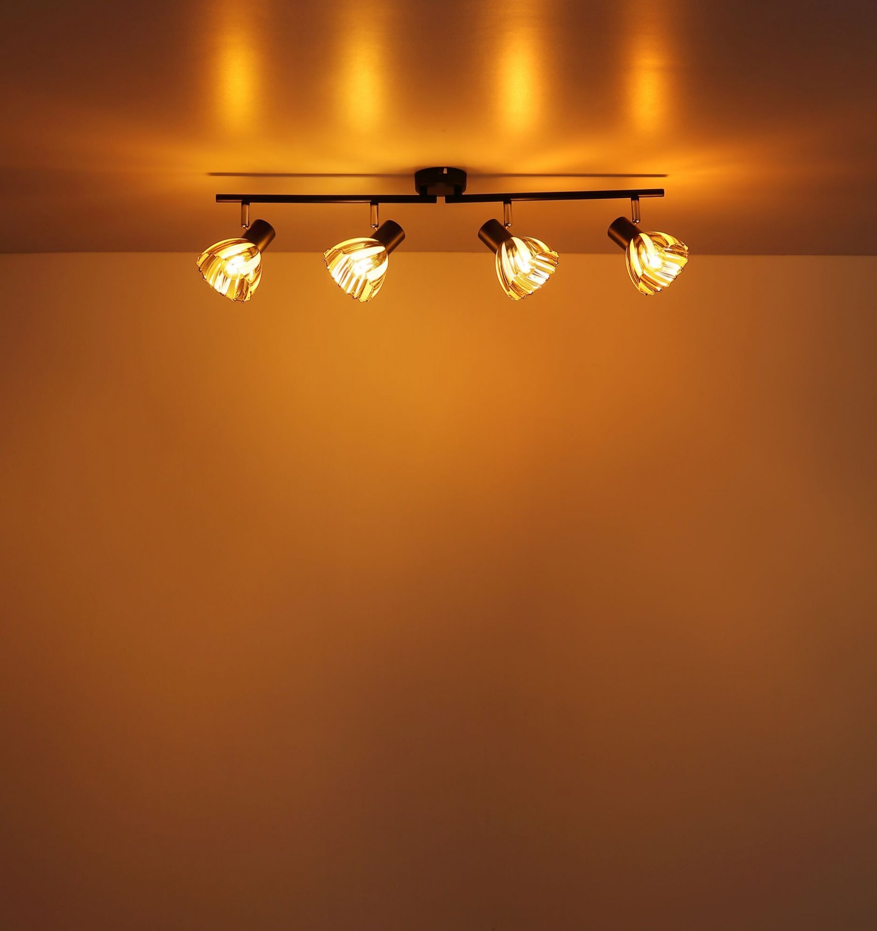 Na suficie zamontowana jest lampa z czterema reflektorami, emitująca ciepłe, żółte światło. Reflektory są skierowane w różnych kierunkach, tworząc przytulną atmosferę.