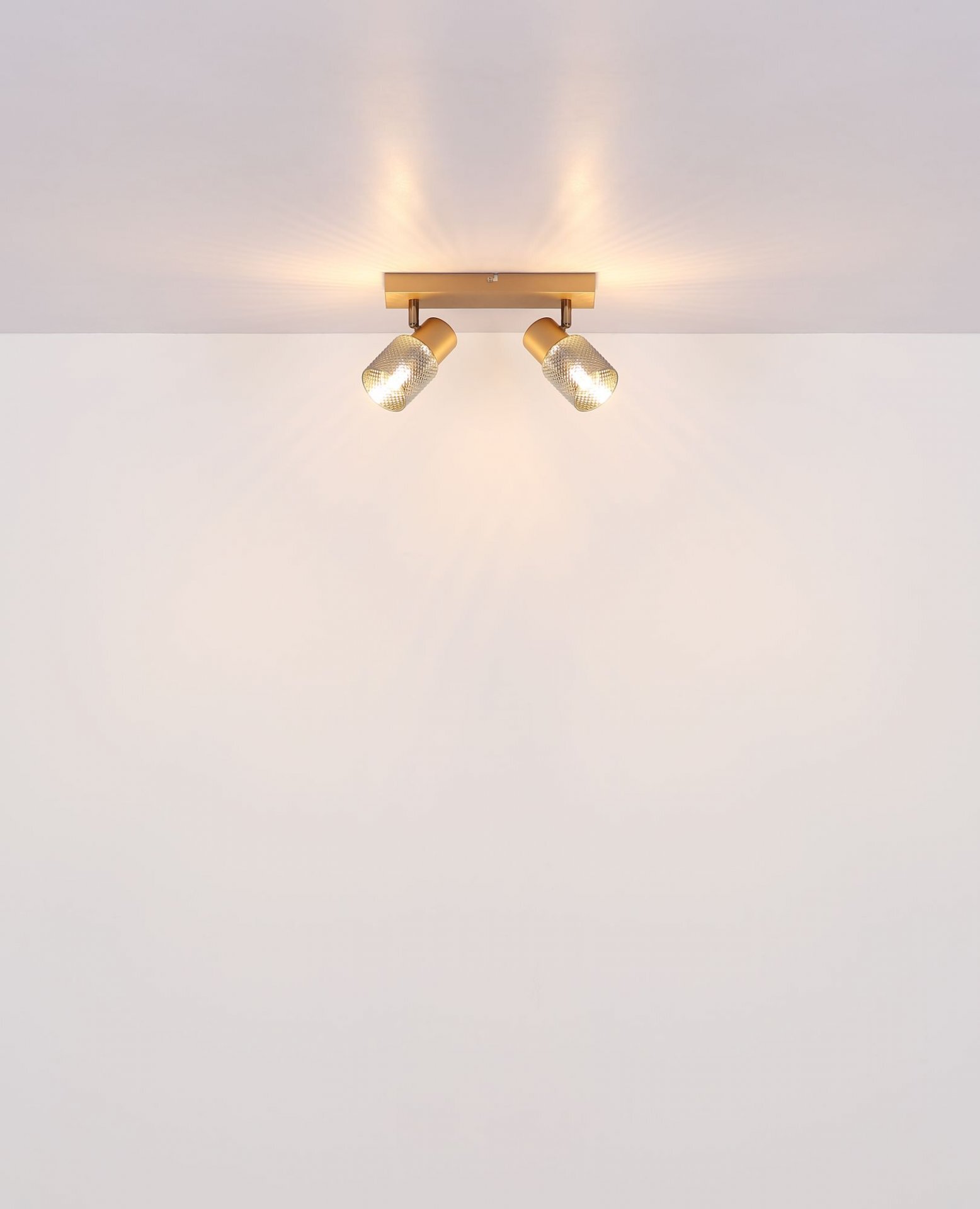 Na suficie zamontowany jest reflektor sufitowy z dwoma punktami świetlnymi, emitującymi ciepłe światło. Reflektor ma nowoczesny design i złoty kolor.