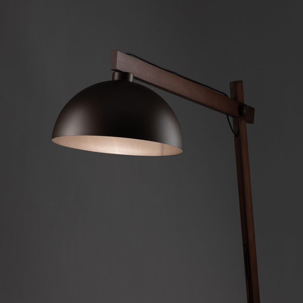 Lampa podłogowa z ciemnym, półokrągłym kloszem i drewnianym ramieniem na ciemnym tle. Klosz jest skierowany w dół, a ramię lampy jest regulowane.