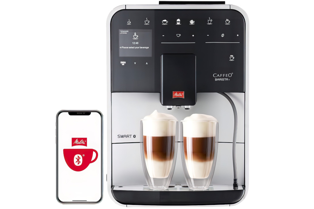 Ekspres do kawy z wyświetlaczem i panelem dotykowym, na którym widoczne są różne ikony napojów oraz tekst \'Please select your beverage\'. Obok ekspresu znajduje się smartfon z logo Melitta i ikoną filiżanki z symbolem Bluetooth.