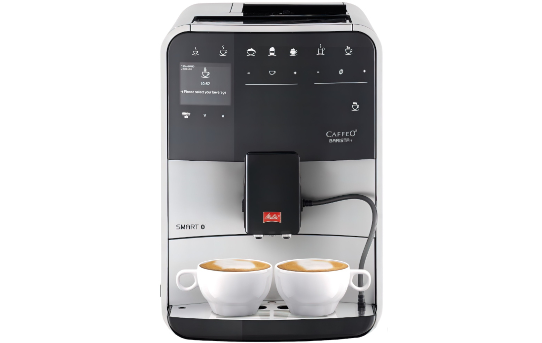 Ekspres do kawy z wyświetlaczem pokazującym godzinę 10:52 i tekst \'Please select your beverage\'. Na dole znajdują się dwie filiżanki z kawą, a na ekspresie widoczne jest logo Melitta.
