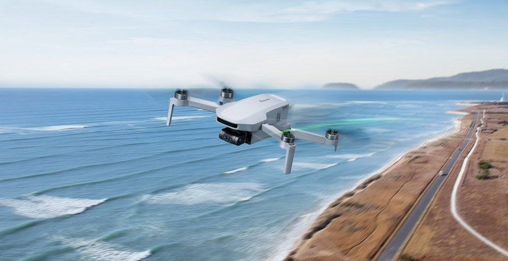 Dron unosi się nad wybrzeżem, z widokiem na morze i linię brzegową. Na dronie widoczne jest logo \'Potensic\'.