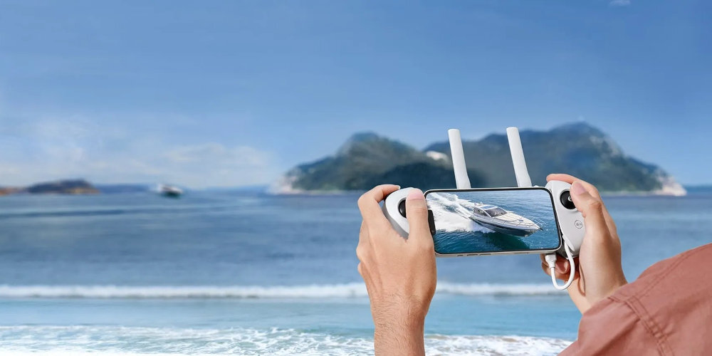 Osoba trzyma kontroler z ekranem, na którym wyświetlany jest obraz łodzi na tle morza i wysp.