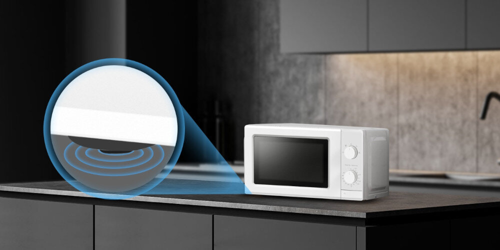 Na blacie kuchennym stoi biała kuchenka mikrofalowa z dwoma pokrętłami. Obok niej widoczna jest grafika przedstawiająca fale mikrofalowe.