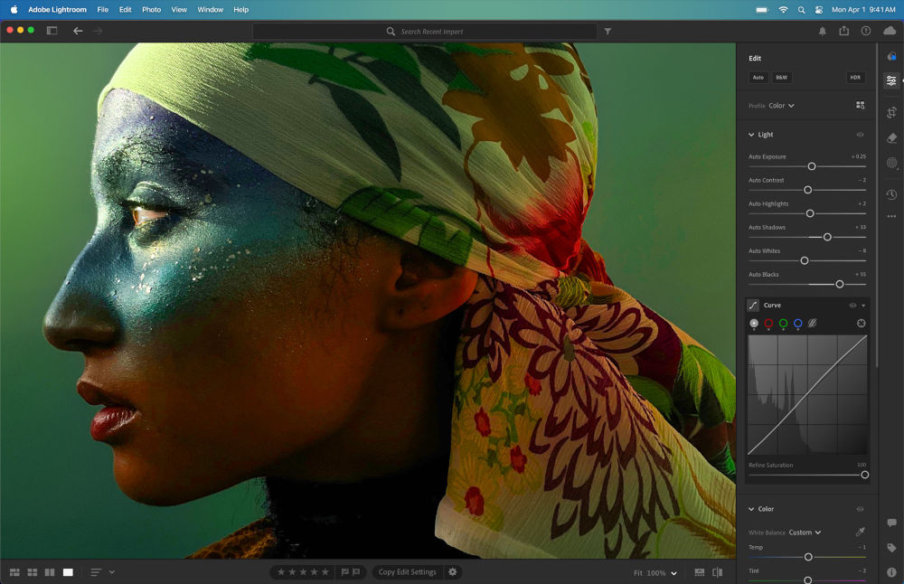 Na ekranie komputera widoczny jest program do edycji zdjęć z obrazem osoby w chustce na głowie, z kolorowym makijażem na twarzy. Po prawej stronie ekranu znajdują się narzędzia edycyjne z suwakami do regulacji parametrów obrazu.