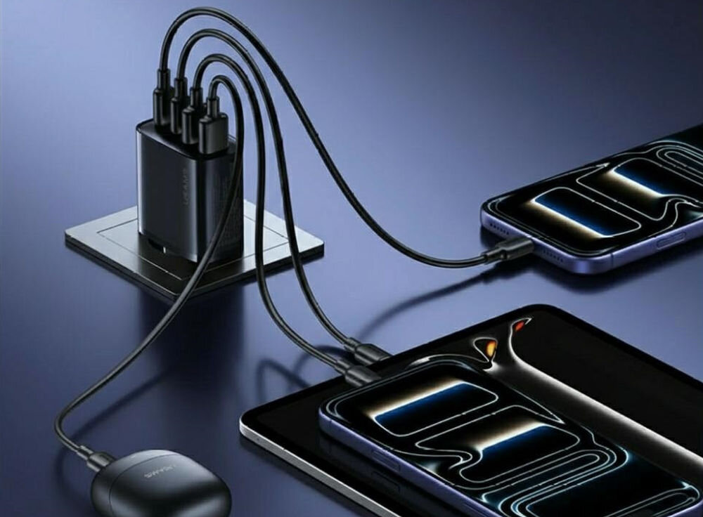 Na obrazie widoczna jest czarna ładowarka sieciowa z kilkoma podłączonymi kablami, które ładują różne urządzenia elektroniczne. Na ładowarce znajduje się napis \'USAMS\'.