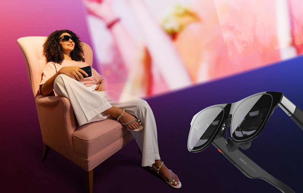 Okulary XREAL One Pro prezentacja funkcjonalności okularów kobieta siedząca na różowym fotelu z założonymi okularami przed nią wyświetlający się ekran pod okulary różowo-fioletowe tło codzienny komfort mniejsze od standardowych modeli AR regulacja rozstawu źrenic dopasowanie do indywidualnej anatomii
