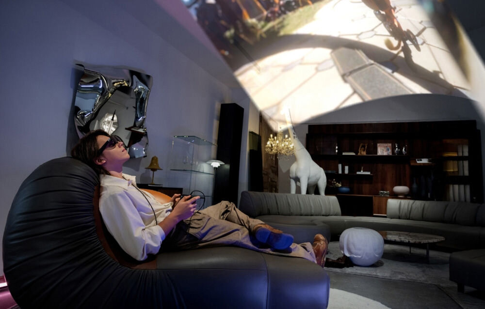 Okulary XREAL One Pro prezentacja funkcjonalności okularów mężczyzna leżący na kanapie ogląda filmik w pokoju dźwięk przestrzenny stworzony przy współpracy z inżynierami Bose czyste zbalansowane i bogate brzmienie Stereo Recording rejestrowanie wyraźnego audio wideokonferencje transmisje na żywo nagrania w terenie